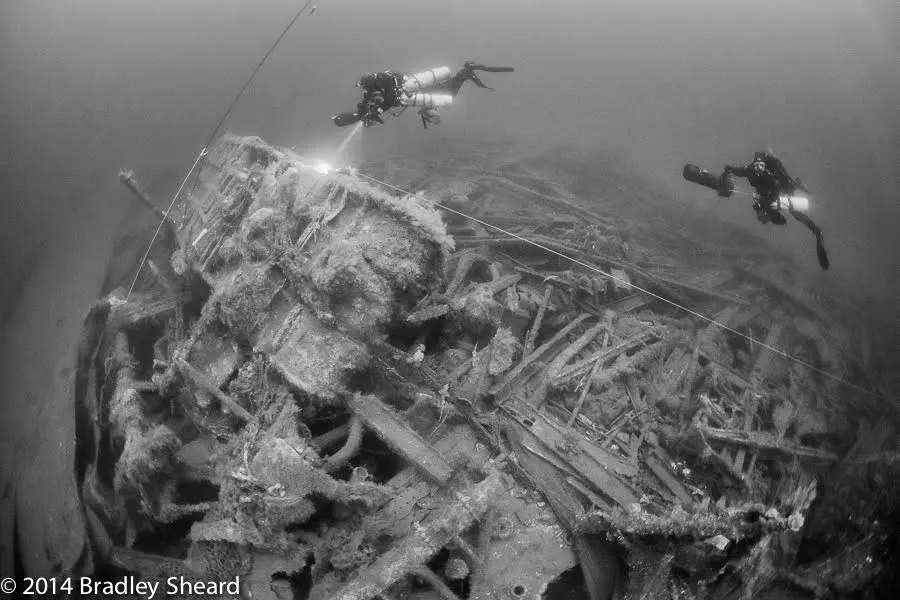 A scuba diver is swimming over the wreckage of an aircraft carrier.