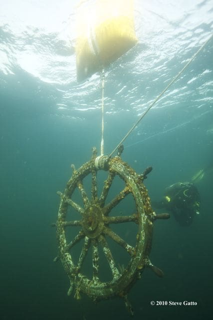 A person in the water with a boat steering wheel.