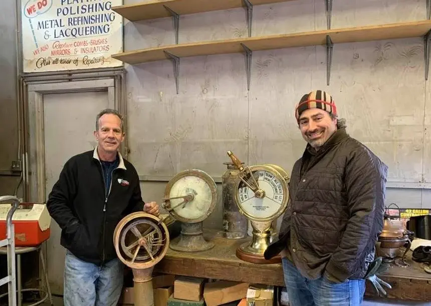 Two men standing next to a table with clocks on it.