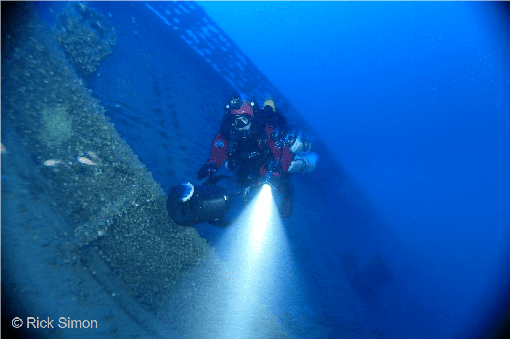 A scuba diver is in the water with his head light on.