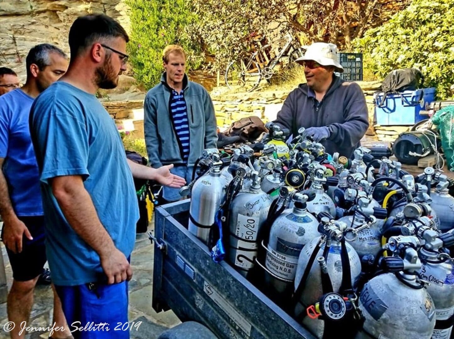 A group of men standing around a truck filled with scuba tanks.