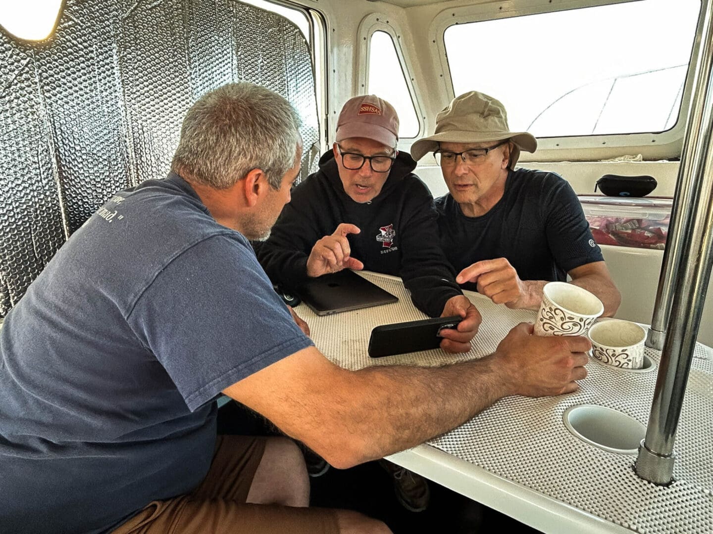 Eric Takakjian (center) reviews underwater footage with Joe Mazraani (right) and Tom Packer before one of the team's dive to measure the engine cylinder. © Jennifer Sellitti 2024